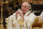 Pope Francis, in his white papal robes,holds a communion wafer while conducting mass in an ornatly decorated Vatican building.