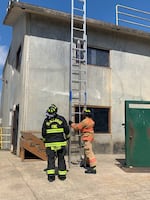 A firefighter props a ladder against a building as another looks on.