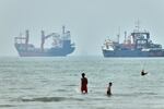 Children wade in the water with cargo ships at anchor in the background and a fisherman nearby, in the Strait of Hormuz off Bandar Abbas, Iran, Tuesday, June 30, 2026.