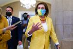Nancy Pelosi walks through a large room wearing a yellow blazer and a face covering