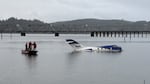 A small plane floats on a body of water on a gray morning. A trio of first responders stand in a boat near the plane.