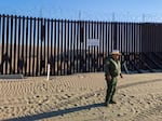 A U.S. Border Patrol agent stands near the border fence, which stretches through the Imperial Sand Dunes in California.