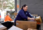 In a blue USPS shirt, a postal worker sorts packages.