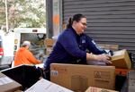 In a blue USPS shirt, a postal worker sorts packages.