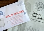 An unopened Oregon ballot envelope for lies on top of a Voters' Pamphlet for the 2026 primary election.