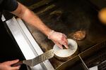 A line cook steams hamburgers on the grill in this May 14, 2020, file photo in Stevenson, Wash. Food producers who sell to retail such as grocery stores have fared well in the pandemic while those who sell to restaurants have struggled.