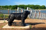 A statue of a large black dog stands by a bridge path down to a riverfront.