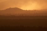 As the setting sun lights up wildfire smoke, a firefighting aircraft flies over the southeast part of the Akawa Butte Fire, burning just north of Sisters, Ore., on July 24, 2026. The Akawa Butte Fire, which is currently the highest priority wildfire in the United States, is burning just north of town.