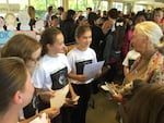 Brooke Abbruzzese (reading from page) and Talia Baskin (red ponytail band) present the girls’ “Saving Pan” cookbook project to Dr. Jane Goodall during a Roots & Shoots event at David Douglas High School in Portland, Oregon, on Oct. 15, 2015. In early 2018, they donated $10,000 from its sales to benefit Goodall’s chimpanzee rehabilitation center and sanctuary in the Republic of Congo.