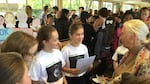 Brooke Abbruzzese (reading from page) and Talia Baskin (red ponytail band) present the girls’ “Saving Pan” cookbook project to Dr. Jane Goodall during a Roots & Shoots event at David Douglas High School in Portland, Oregon, on Oct. 15, 2015. In early 2018, they donated $10,000 from its sales to benefit Goodall’s chimpanzee rehabilitation center and sanctuary in the Republic of Congo.