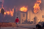 A man wearing a red shirt and grey shorts walks towards a church on fire, surrounded by smoke.