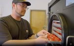 A white man with glasses wearing a black baseball cap and black t-shirt loads a tray of strawberries into a freeze dryer.