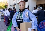 Wanda Bright holds a cardboard box of food as volunteers provide food to others standing in line.