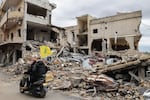 Men ride a scooter with a Hezbollah flag past destroyed buildings as people make their way back to their homes in the south of Lebanon after a ceasefire between Israel and Hezbollah took effect, on November 27, 2024, in the southern town of Qana.
