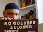 Dr. Khalid el-Hakim holds a cast iron "No Colored Allowed" theater sign from 1925.