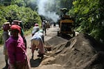 TOPSHOT - This photograph taken on March 26, 2026 shows construction workers operating a smoke-spewing tarmac mixer to build a road cutting through forest land, as part of the Great Nicobar Island Project, a government-backed mega-development undertaking on the outskirts of Campbell Bay in Great Nicobar Island. On a remote island in the Andaman Sea, bulldozers are tearing into pristine forests home to one of Earth's most isolated people -- part of India's ambition for a $9 billion megaport, airport and city. Designed to rival China's investments around the Indian Ocean, New Delhi's colossal project will be built on Great Nicobar Island, a site offering a naval presence far closer to Southeast Asia than India's mainland. (Photo by R. Satish BABU / AFP via Getty Images) / TO GO WITH 'India-Nicobar-Politics-Environment-Economy' FOCUS
