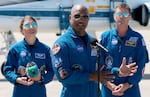 Artemis II crew members — mission specialist Christina Koch (left) and commander Reid Wiseman (right) — listen as pilot Victor Glover speaks to the media after arriving at the Kennedy Space Center on March 27, 2026 in Cape Canaveral, Florida. The astronauts' planned 10-day mission will take them around the Moon and back to Earth.
