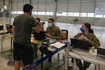 A person in a green shirt and black shorts talks to three people in camo Air Force uniforms.