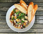 A bowl of clams in broth with chopped greens and bread.