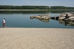 A man walks on the sandbank by the wreckage of a WWII German warship, emerged due to the drought, in front of Djerdap II, a large dam on the Danube River, between Romania and Serbia, near Prahovo, Serbia, Tuesday, Aug. 4, 2026.