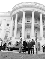 As President Harry Truman and General Dwight Eisenhower greet military officials at the White House in June 1952, First Lady Bess Truman and First Daughter Margaret Truman hang over the railing on the upper balcony.