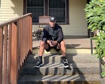 A man sits on the front stairs of a little yellow house