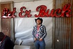 A man with a complete cowboy outfit poses underneath a bright red sign in a tent.