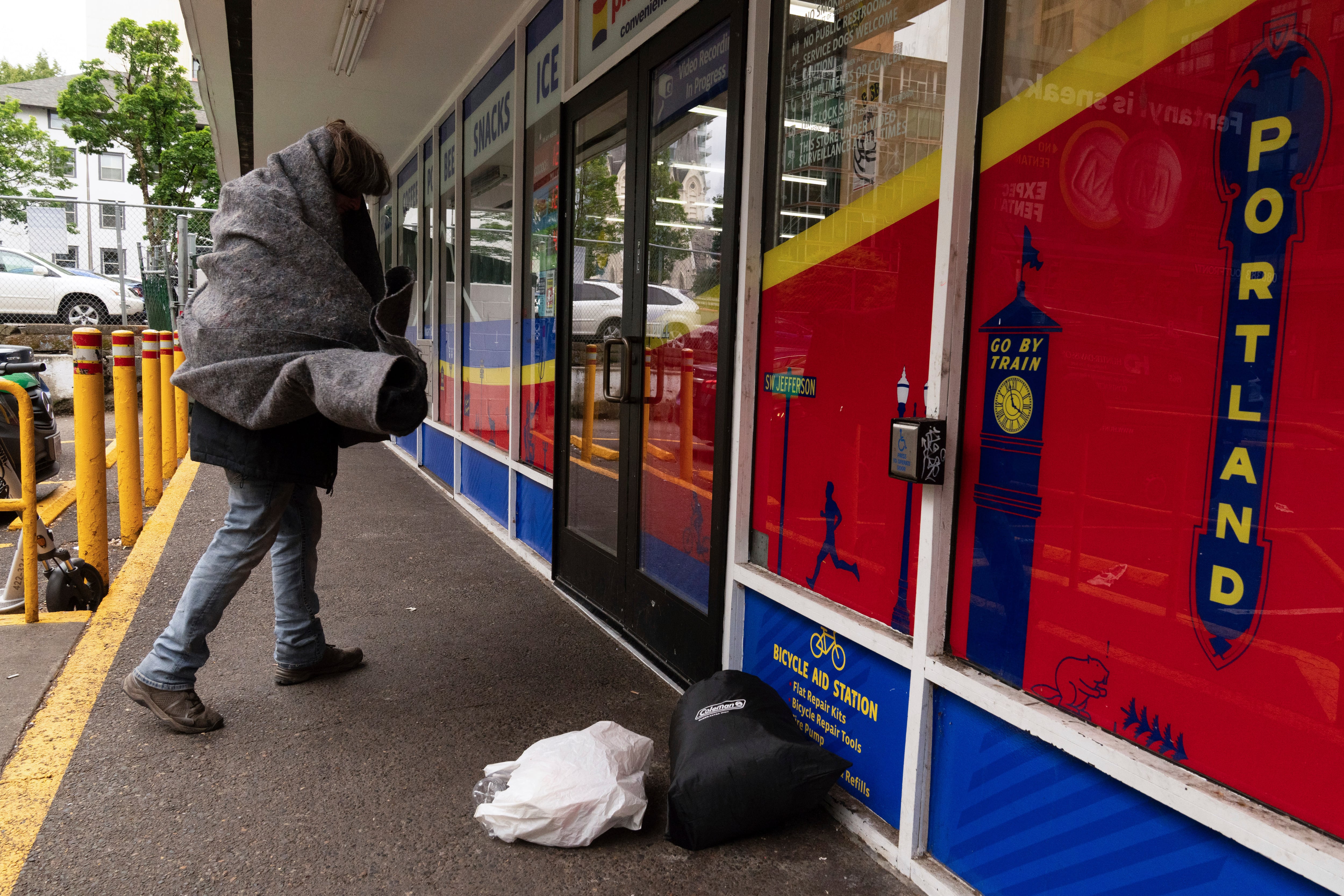 A homeless man walks into a Plaid Pantry convenience store after his bag of bottles, bottom center, was denied for collection in Portland, Ore.