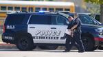Two police officers walk in front of a police SUV with a blurry school bus in the background.