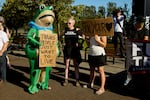 A woman and a man dressed in a frog costume hold signs supporting trans people during a rally to support Indiana Fever guard Sophie Cunningham after her comments on transgender athletes in women's sports before a WNBA basketball game between the Portland Fire and the Indiana Fever in Portland, Ore., Friday, July 31, 2026.