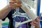 A man in a Metallica T-shirt holds up an aluminum airplane part, painted white. It was created by one of his students.