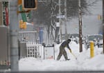 A man shovels snow on a commercial street. 