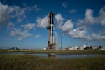 A rocket sits on a launchpad with watery habitat in the foreground.