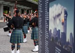 Portland Fire Fighters Pipes and Drums, left, perform at Tom McCall Waterfront Park, marking the 25th anniversary of the terrorist attacks on Sept. 11, 2001. At right is a display showing names of the victims surrounding an image of the World Trade Center’s South Tower on fire.
