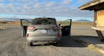 A grey car parked in a gravel lot, with an informational sign at the right. The back of the car reads Lake County Public Transit.