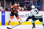 Philadelphia Flyers' Sean Couturier, left, passes the puck against Seattle Kraken's Yanni Gourde (37) during the third period of an NHL hockey game, Saturday, Feb. 10, 2024, in Philadelphia.