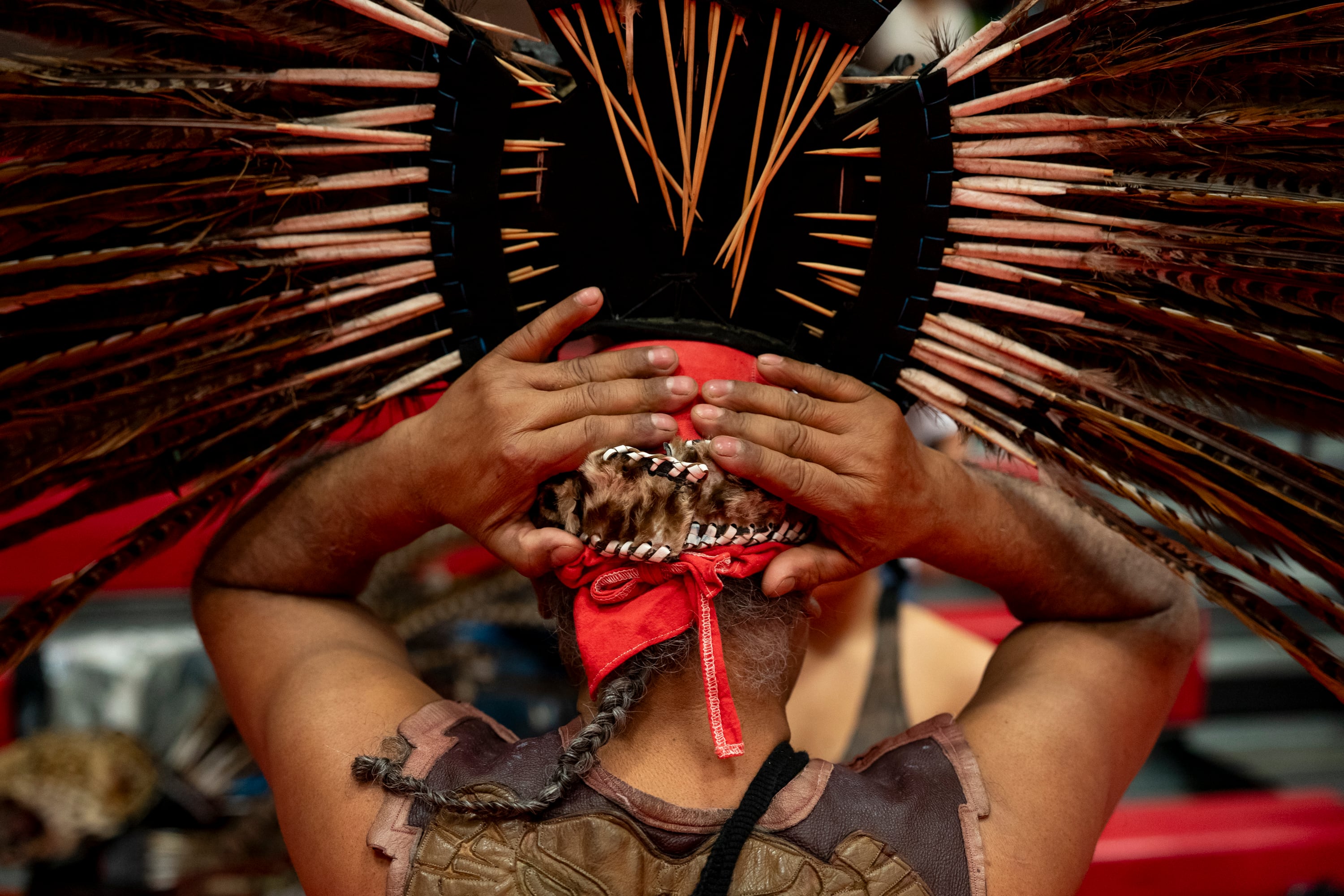 Jaime Uribe, a Mexica Aztec man, puts on his headdress made of red pheasant feathers and a jaguar head at the Veterans Powwow at Chemawa Indian School in Salem, Ore., on Nov. 8, 2025.