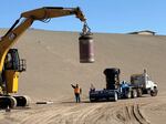 Crews use a flatbed truck to drive the containers down to the disposal cell. Then, using a specialized grapple, they remove the stainless steel containers holding vitrified tank waste from their black protective sleeves.