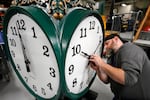 A technician adjusts clock hands on a large outdoor clock under construction.