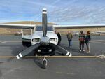 Three people stand near an aircraft on tarmac.