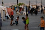 People walk past tents set up as temporary shelters by displaced families fleeing the Israeli airstrikes in the south and Dahiyeh, on Beirut's corniche, Lebanon, Monday, Oct. 14, 2024.