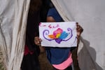 A girl at Roj holds a picture of a flower that she painted. On the back, it says, "hello friends."