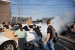 Pro-immigration demonstrators try to stop a car leaving an ICE processing center during a protest in Broadview, Ill., on Sept. 19, 2025. A white cloud appears behind the car.
