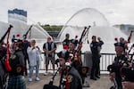 Attendees and Portland firefighters watch Portland Fire Fighters Pipes and Drums perform as a Portland Fire & Rescue's fire boats spray water on the Willamette River.