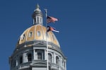 The U.S. and Colorado state flag fly in front of the dome at the Colorado State Capital in Denver in 2025.
