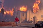 A man walks in front of the burning Altadena Community Church, Wednesday, Jan. 8, 2025, in the downtown Altadena section of Pasadena, Calif.