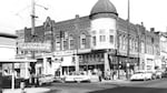A black-and-white photo shows a bustling business district with a lunch counter, drug store, cafe, dry cleaner and other community services.