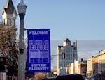 A blue sign on a lightpost states "Welcome Historic Baker City". The historic Geiser Grand Hotel and Baker Tower loom in the background.