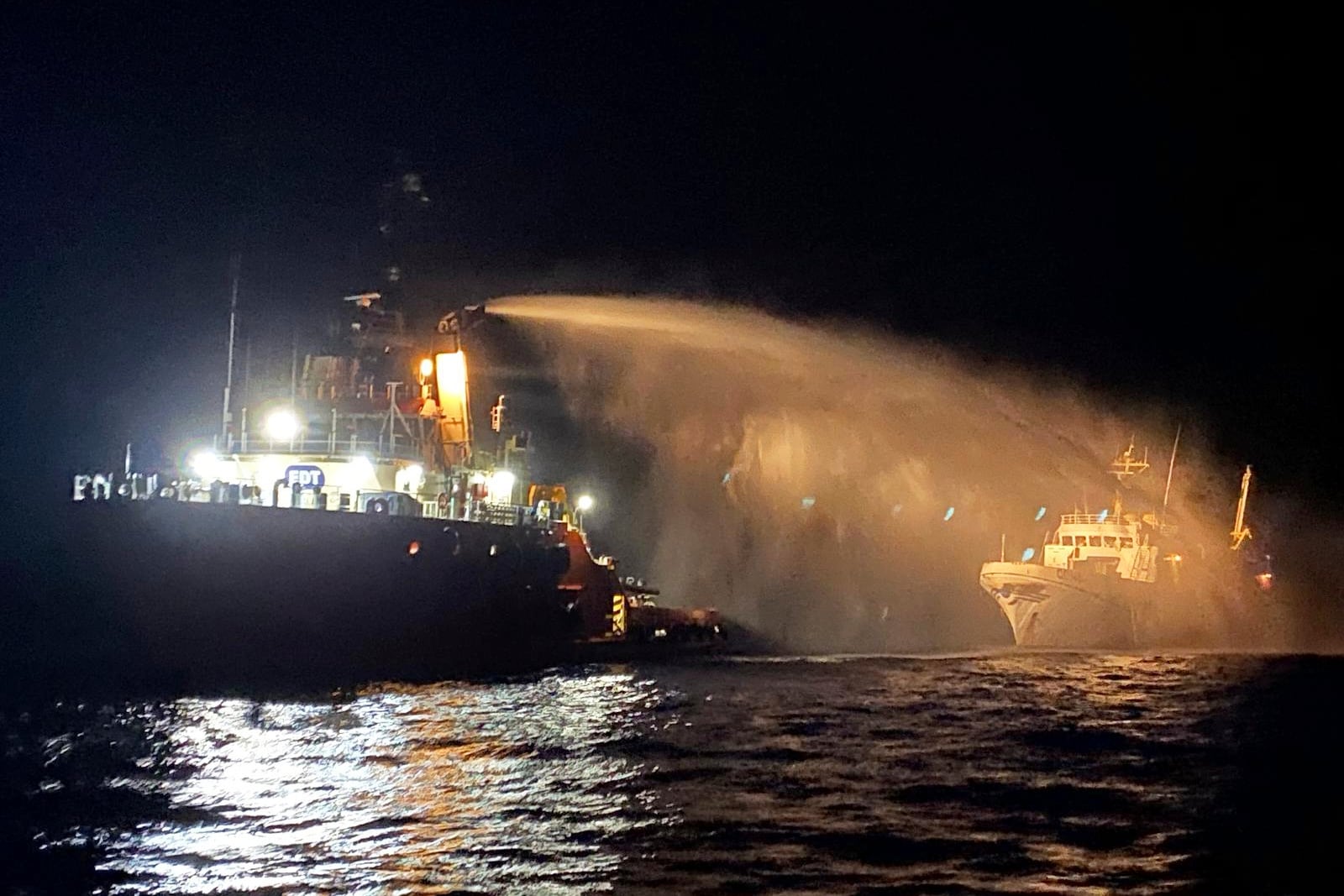 A firefighting-equipped tug boat, left, contacted by the Malta Vessel Traffic Services (VTS) helps controlling a fire occurred on the bow of the Conscience vessel in international waters of the Mediterranean Sea, Friday, May 2, 2025.