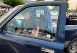 A man gets into the driver seat of a small blue pickup truck. He is smiling.